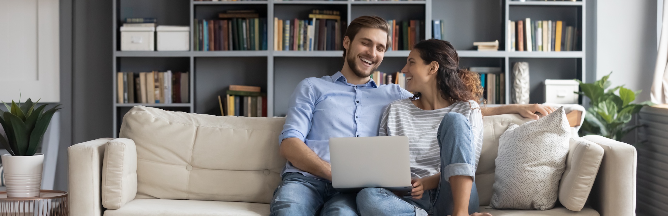 happy couple sitting on couch using laptop